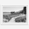 A fine art black and white vintage style framed photography print featuring a rustic old boathouse nested on a Lake Tahoe beach.