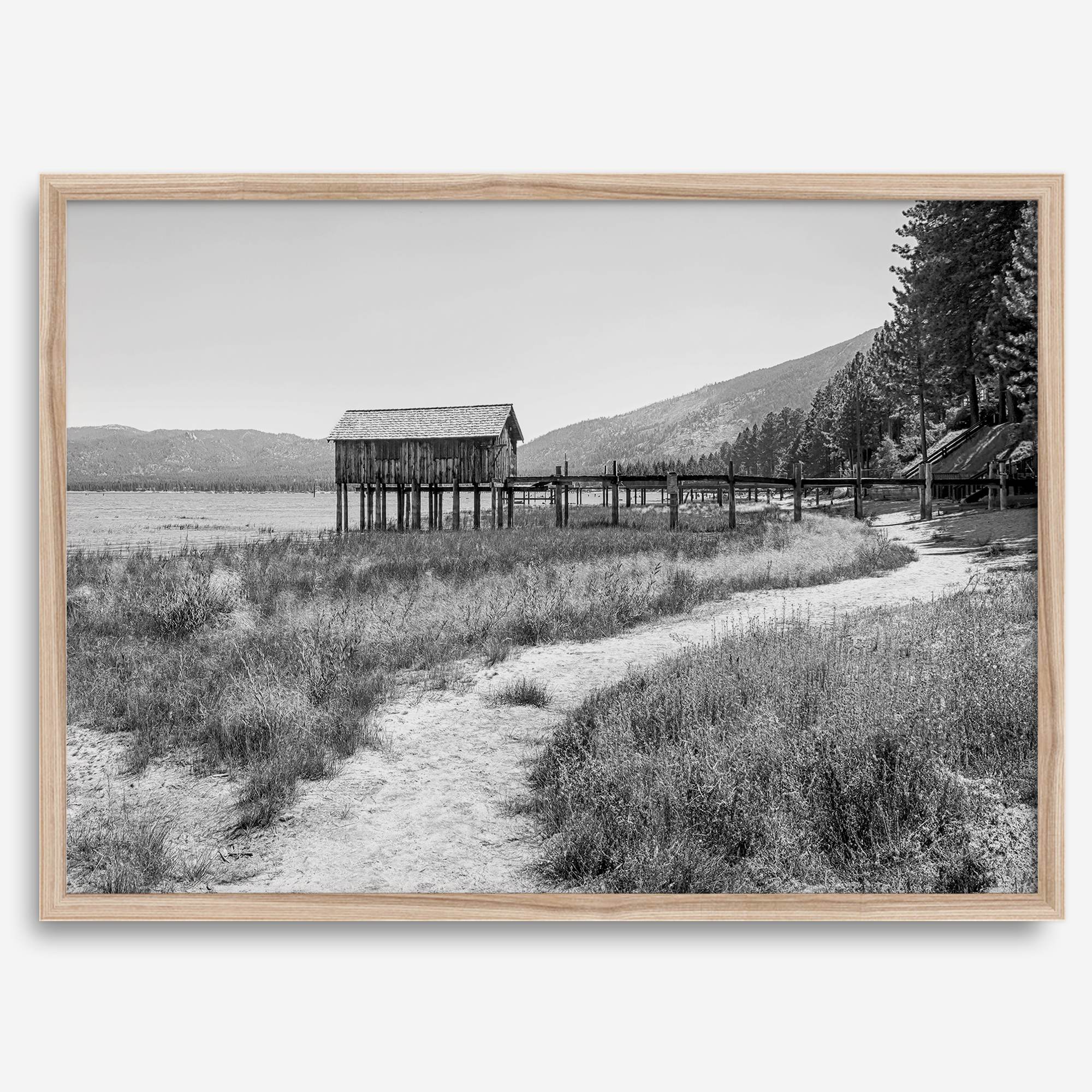 A fine art black and white vintage style framed photography print featuring a rustic old boathouse nested on a Lake Tahoe beach.
