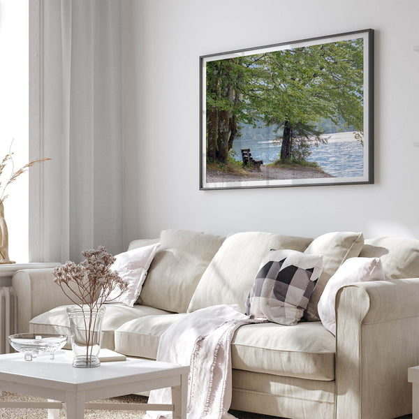 Framed serene lake print showing a bench by the water under lush green trees, with soft sunlight reflected on the calm lake surface.
