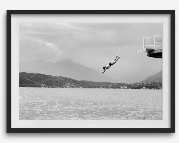 Diver leaping from a platform over a serene Austrian lake, with misty mountains in the background.