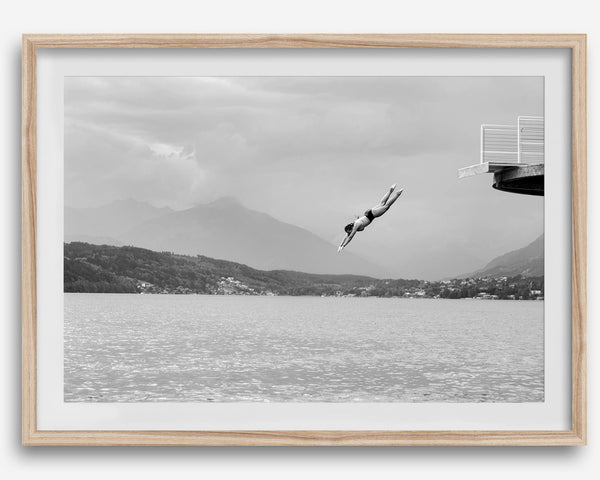 Diver leaping from a platform over a serene Austrian lake, with misty mountains in the background.