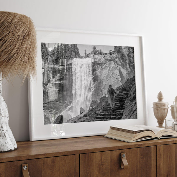 Climb the breathtaking Mist Trail in Yosemite National Part with this fine art black and white waterfall nature print. This nature landscape wall art showcases the stunning gushing waterfall and the people scaling the trail with their colorful raincoats.