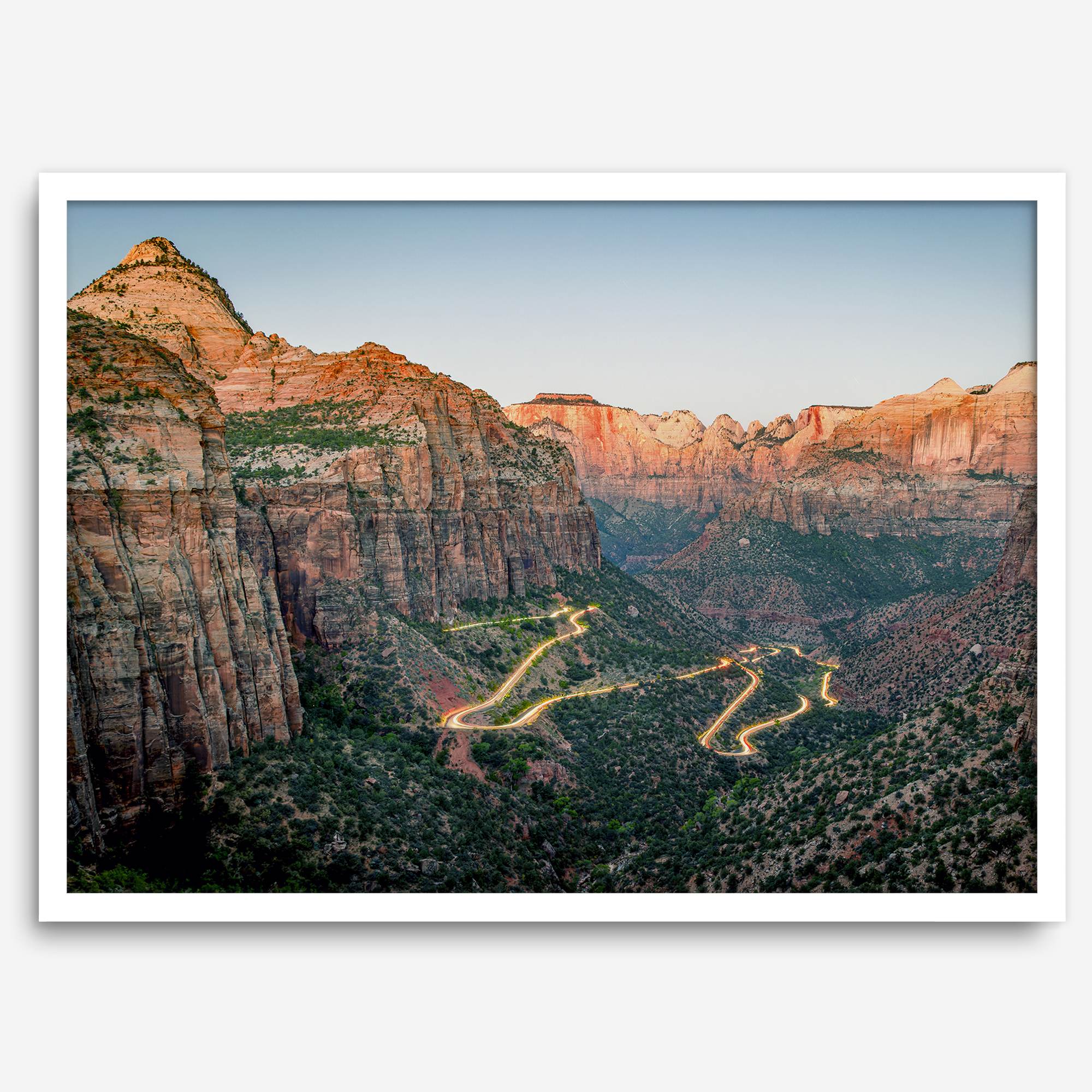 Framed Zion National Park print with winding road illuminated through red cliffs and majestic canyon scenery at dusk.
