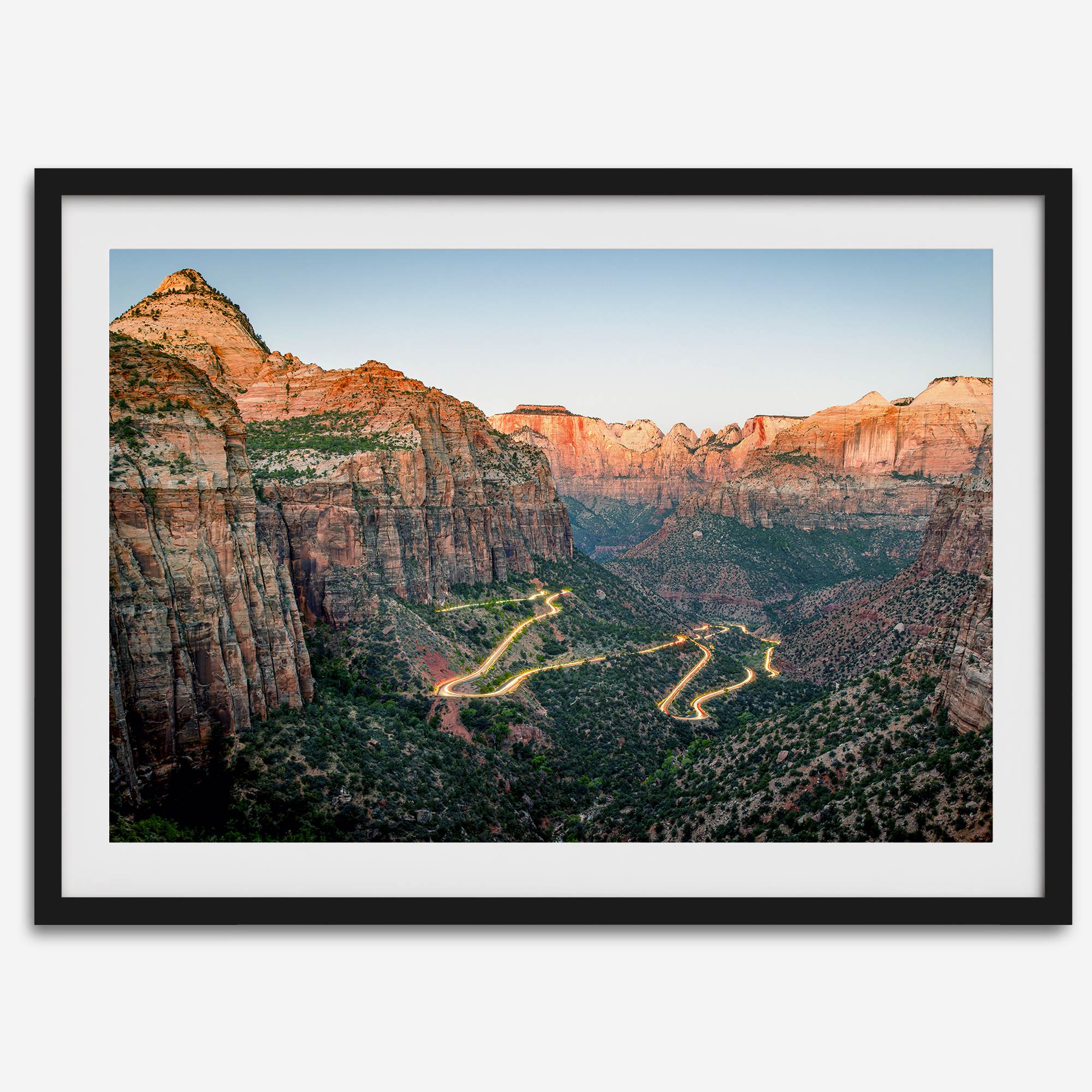 Framed Zion National Park print with winding road illuminated through red cliffs and majestic canyon scenery at dusk.