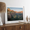 Framed Zion National Park print with winding road illuminated through red cliffs and majestic canyon scenery at dusk.