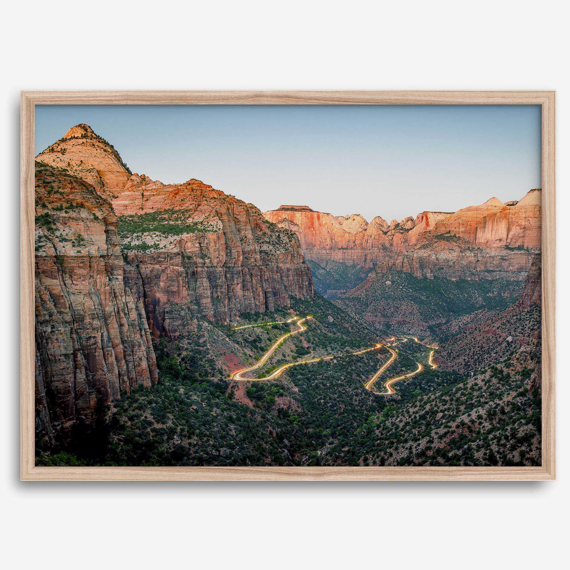 Framed Zion National Park print with winding road illuminated through red cliffs and majestic canyon scenery at dusk.