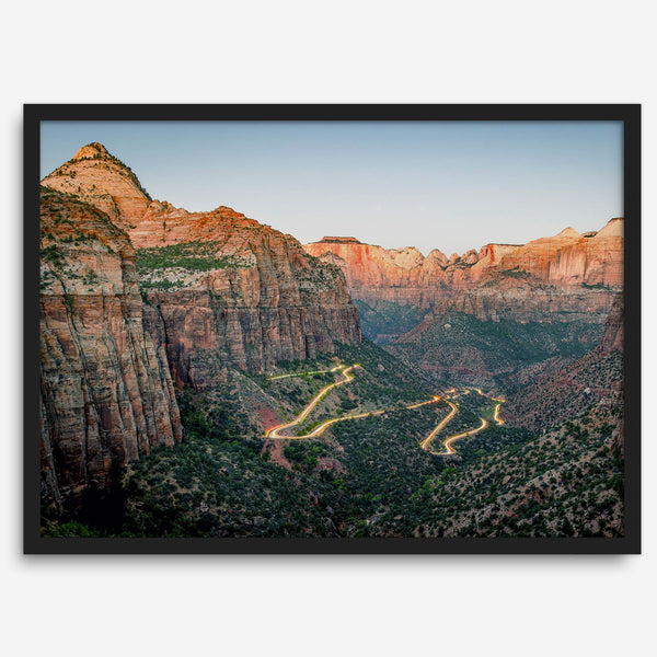 Framed Zion National Park print with winding road illuminated through red cliffs and majestic canyon scenery at dusk.