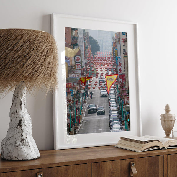 Red lanterns line Grant Avenue in San Francisco’s Chinatown, framed by colorful signs and bustling city life. Available as a framed or unframed print.