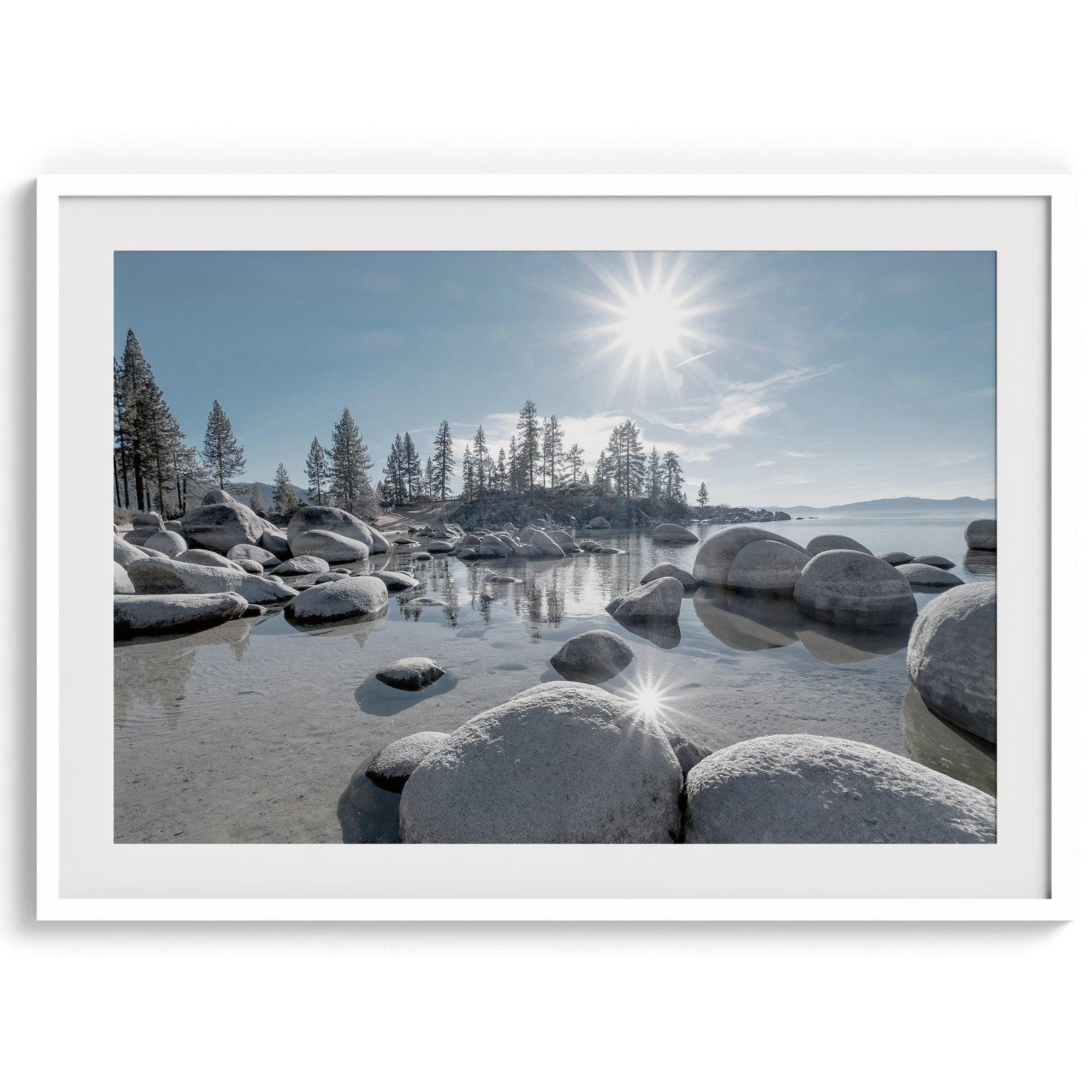 Capture the beauty of Lake Tahoe with this stunning lake wall art. The image showcases majestic rocks rising from crystal-clear water, contrasting with the blue sky. The sun's reflection adds a warm, magical touch to the breathtaking scenery.