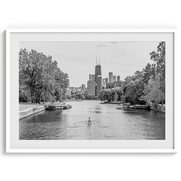 Black and white photo of Lincoln Park, Chicago. A lone rower glides on the park canal with the iconic Willis Tower (formerly Sears Tower) and Chicago skyline in the background.