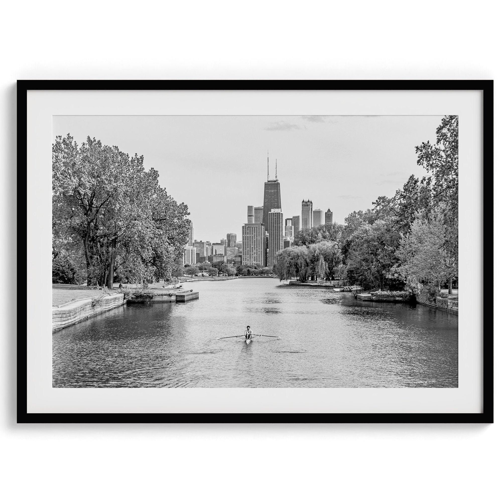 Black and white photo of Lincoln Park, Chicago. A lone rower glides on the park canal with the iconic Willis Tower (formerly Sears Tower) and Chicago skyline in the background.