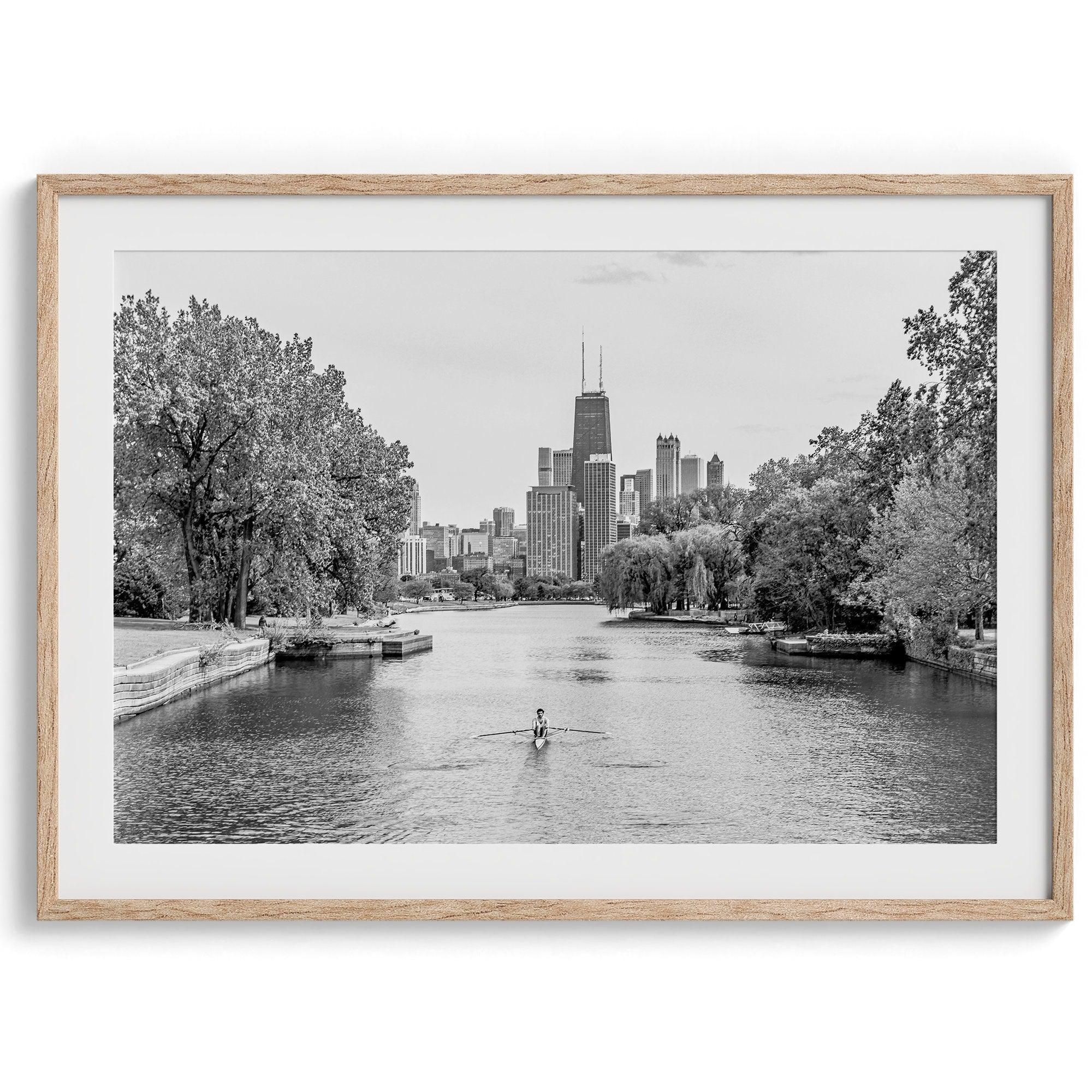 Black and white photo of Lincoln Park, Chicago. A lone rower glides on the park canal with the iconic Willis Tower (formerly Sears Tower) and Chicago skyline in the background.