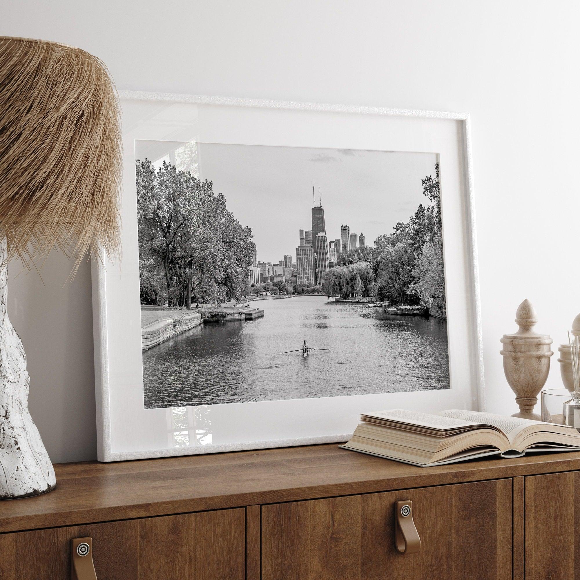 Black and white photo of Lincoln Park, Chicago. A lone rower glides on the park canal with the iconic Willis Tower (formerly Sears Tower) and Chicago skyline in the background.