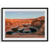 Landscape photo of Reflection Canyon in the Utah desert at sunset, with fiery red hues reflected in still water below a blue sky with a moon.