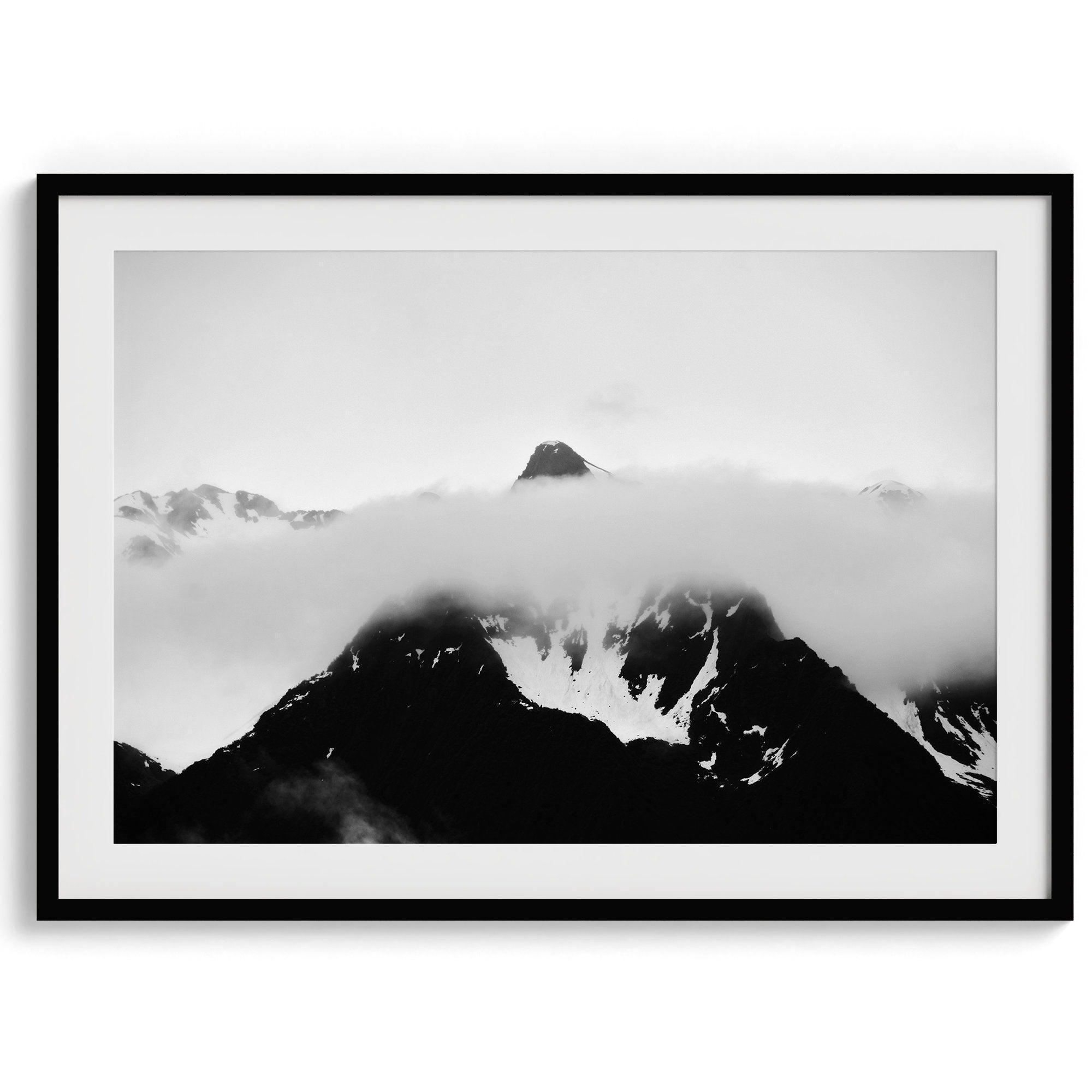 Dramatic black and white landscape of a peak in Alaska, its top rising above a layer of clouds.