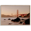 Limited-edition print: Golden Gate Bridge at sunset. Long exposure blurs ocean waves, contrasting with fiery red & orange sky. Dramatic scene with bridge framed by foreground rocks.