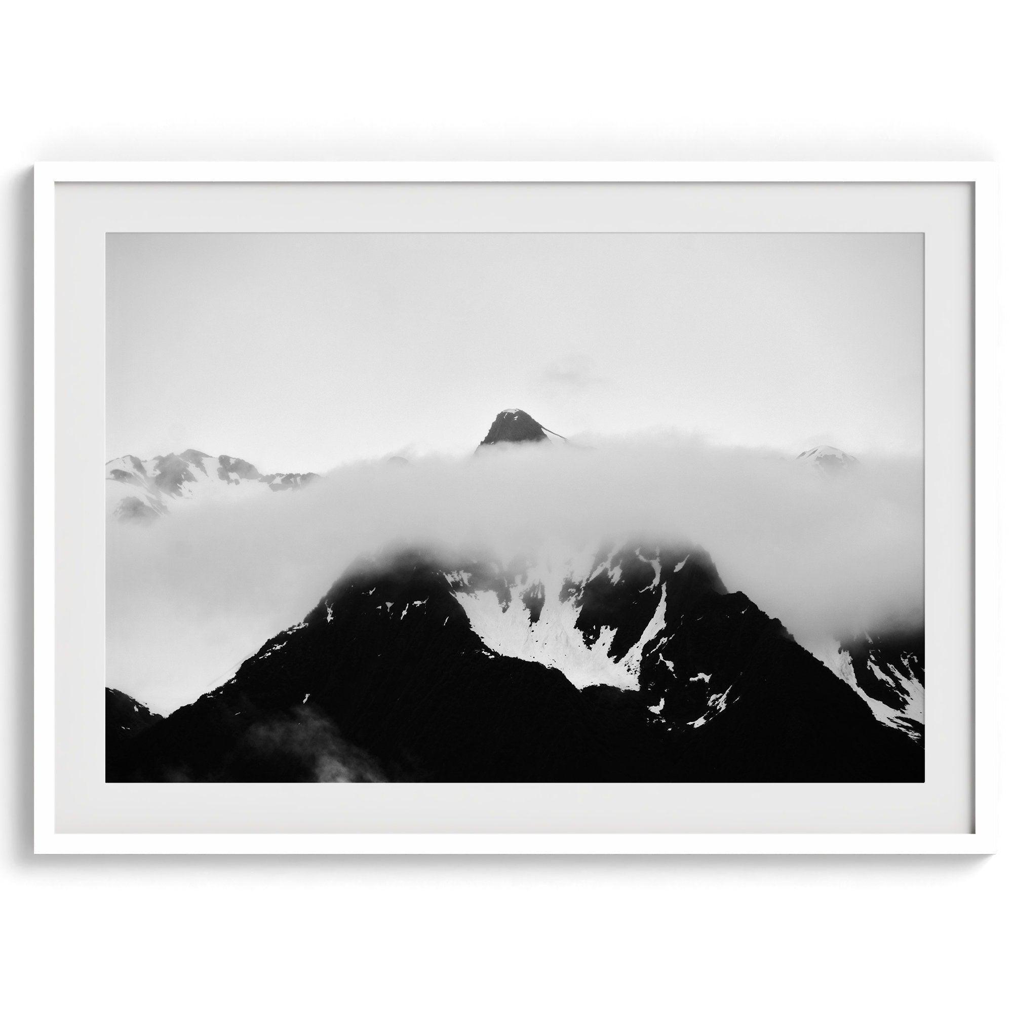 Dramatic black and white landscape of a peak in Alaska, its top rising above a layer of clouds.