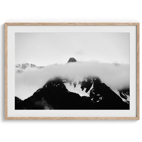 Dramatic black and white landscape of a peak in Alaska, its top rising above a layer of clouds.