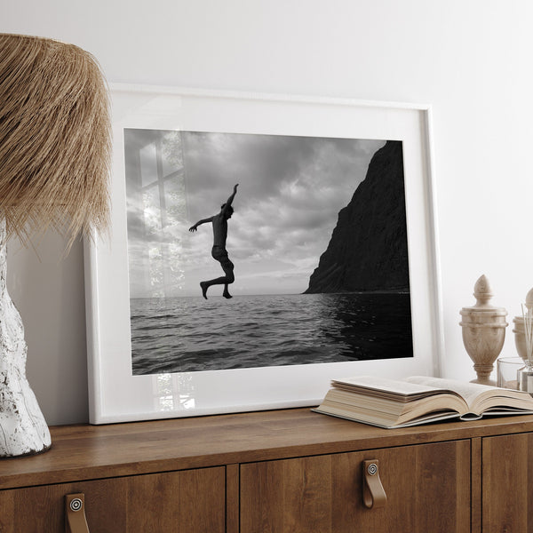 A black and white fine art ocean photography print showing a young carefree adult diving into the sea in Kauai, Hawaii. This ocean lifestyle scene makes it look like this person is walking on water.