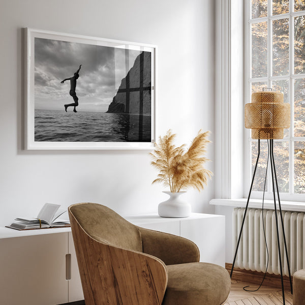 A black and white fine art ocean photography print showing a young carefree adult diving into the sea in Kauai, Hawaii. This ocean lifestyle scene makes it look like this person is walking on water.