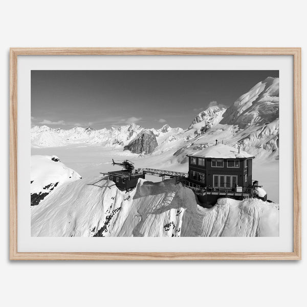 Black and white mountain cabin wall art with helicopter over snowy Denali peaks, Alaska winter landscape photography print.