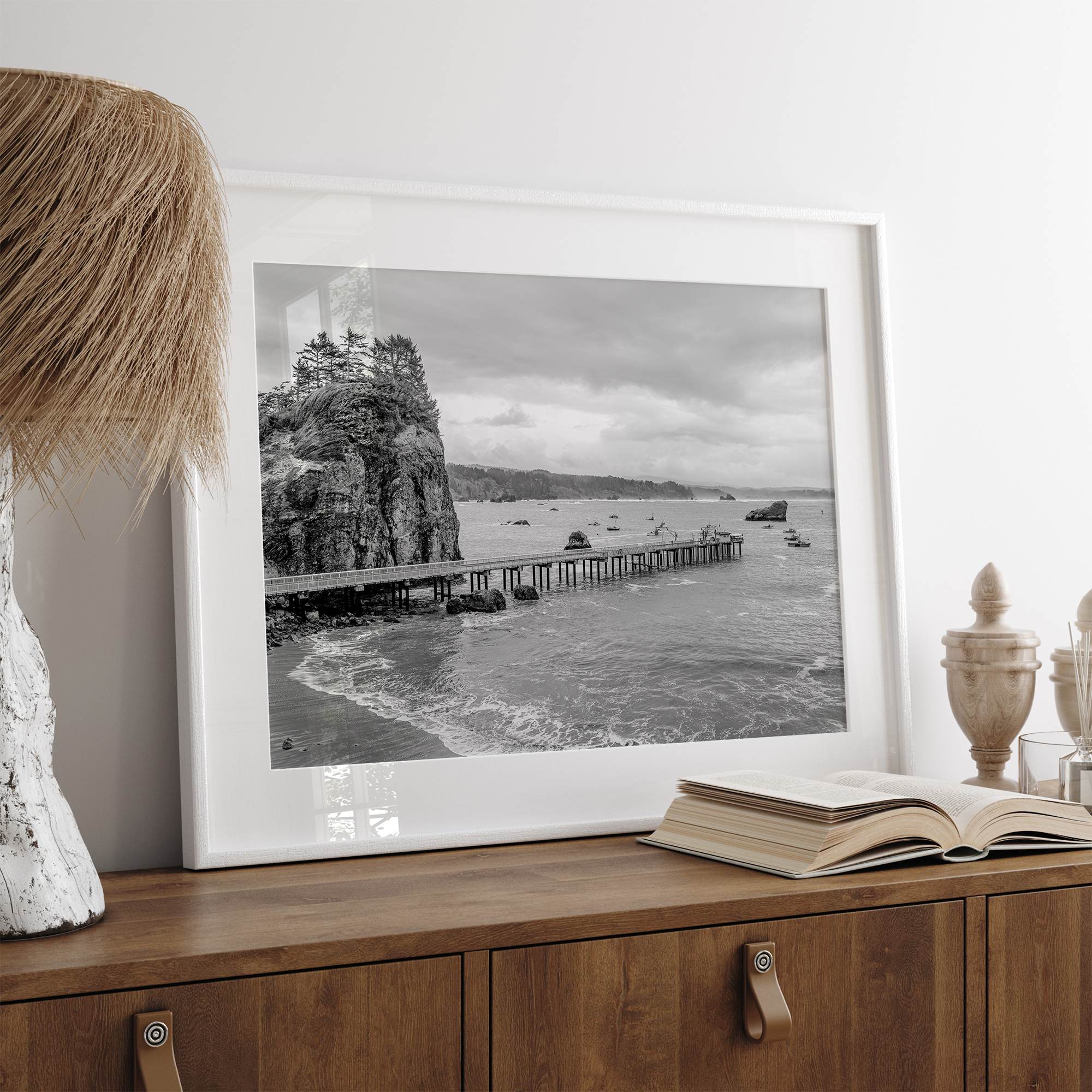 Scenic Pacific Northwest wall art of Trinidad State Park in California in black and white, showcasing a coastal pier, lush green cliffs, and calm ocean waves under cloudy skies.