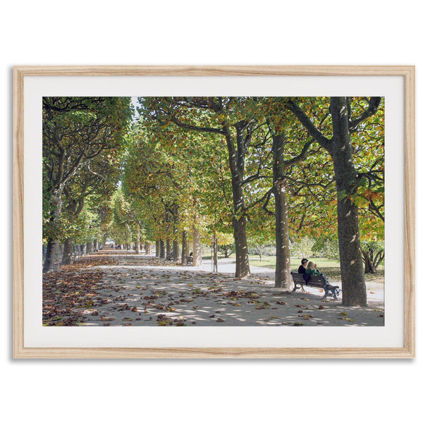 A fine art Paris print of Jardin des Tuileries in fall, featuring a couple sitting on a bench beneath vibrant autumn trees, surrounded by golden foliage.