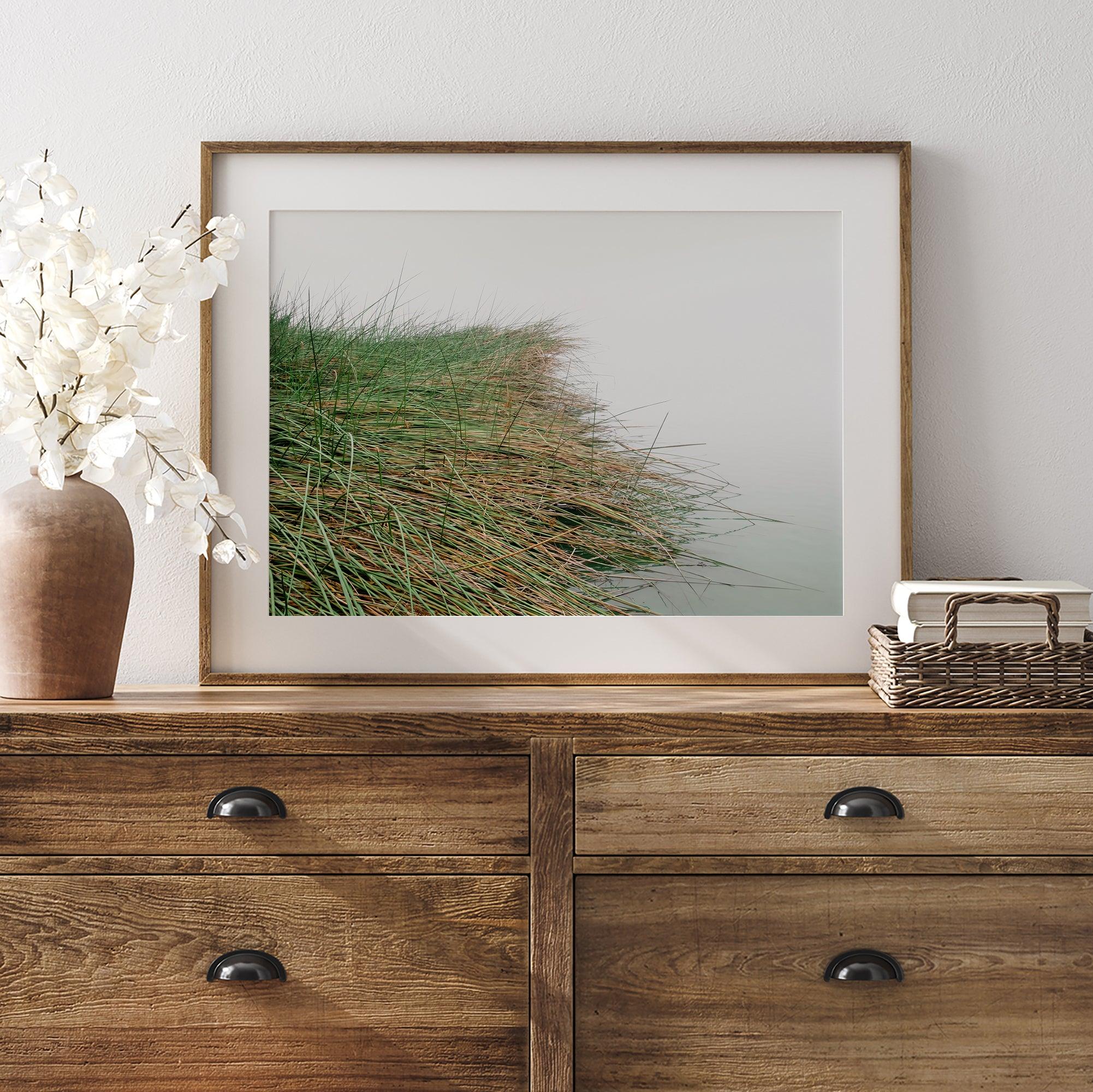 Minimalist nature artwork of coastal grasses leaning towards calm water on a misty day