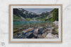 A framed fine art landscape print of a crystal-clear blue lake in Washington State. The tranquil water reveals colorful rocks beneath the surface, with snow-capped mountains towering in the distance.