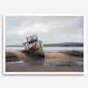 Weathered shipwreck resting on a quiet coastal shore, surrounded by marshland and a moody, overcast sky.