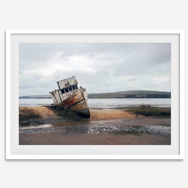 Weathered shipwreck resting on a quiet coastal shore, surrounded by marshland and a moody, overcast sky.