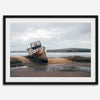 Weathered shipwreck resting on a quiet coastal shore, surrounded by marshland and a moody, overcast sky.