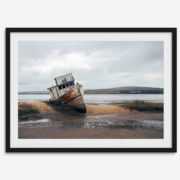 Weathered shipwreck resting on a quiet coastal shore, surrounded by marshland and a moody, overcast sky.