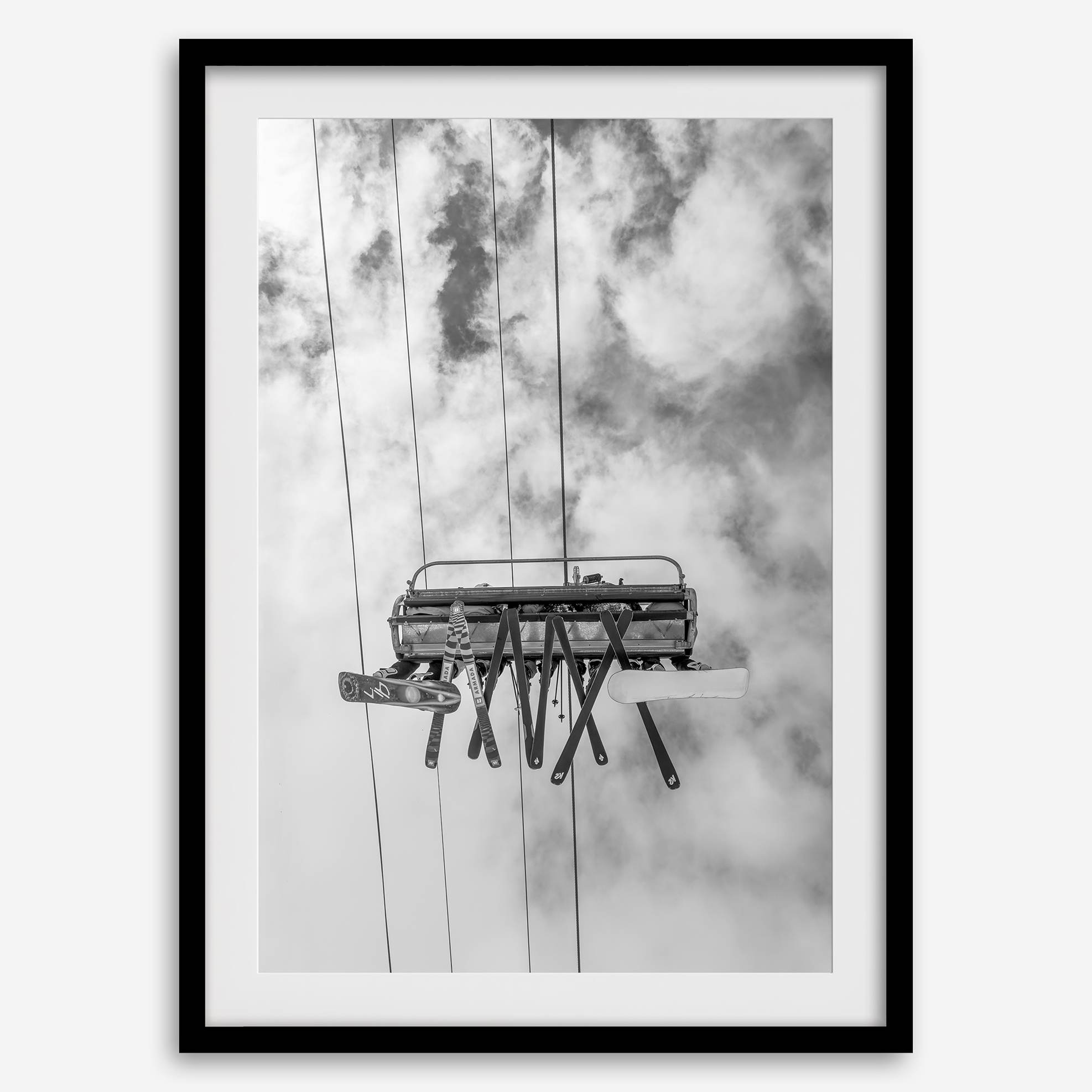 Monochrome ski lift view from below with hanging skis and cloudy mountain sky background.