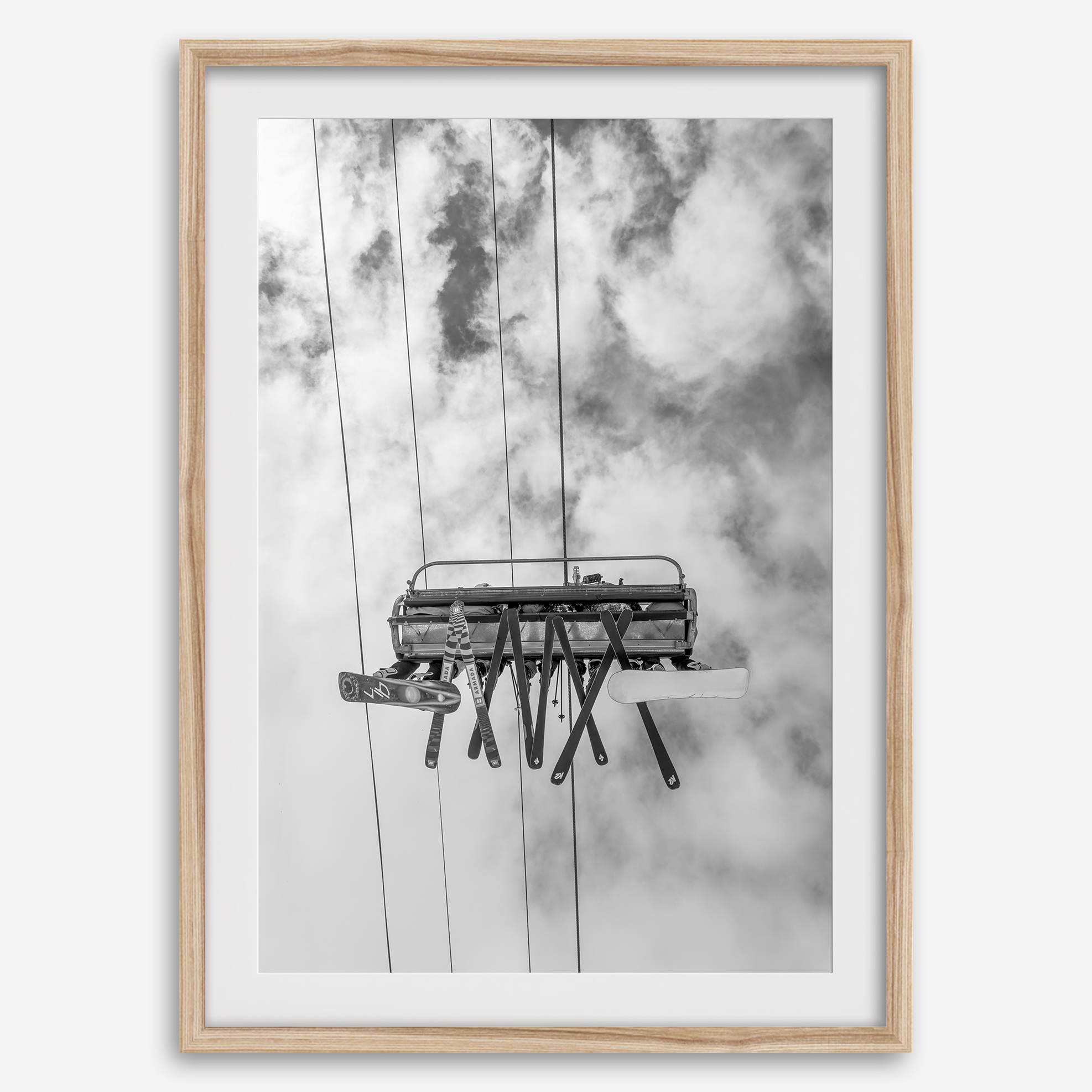 Monochrome ski lift view from below with hanging skis and cloudy mountain sky background.