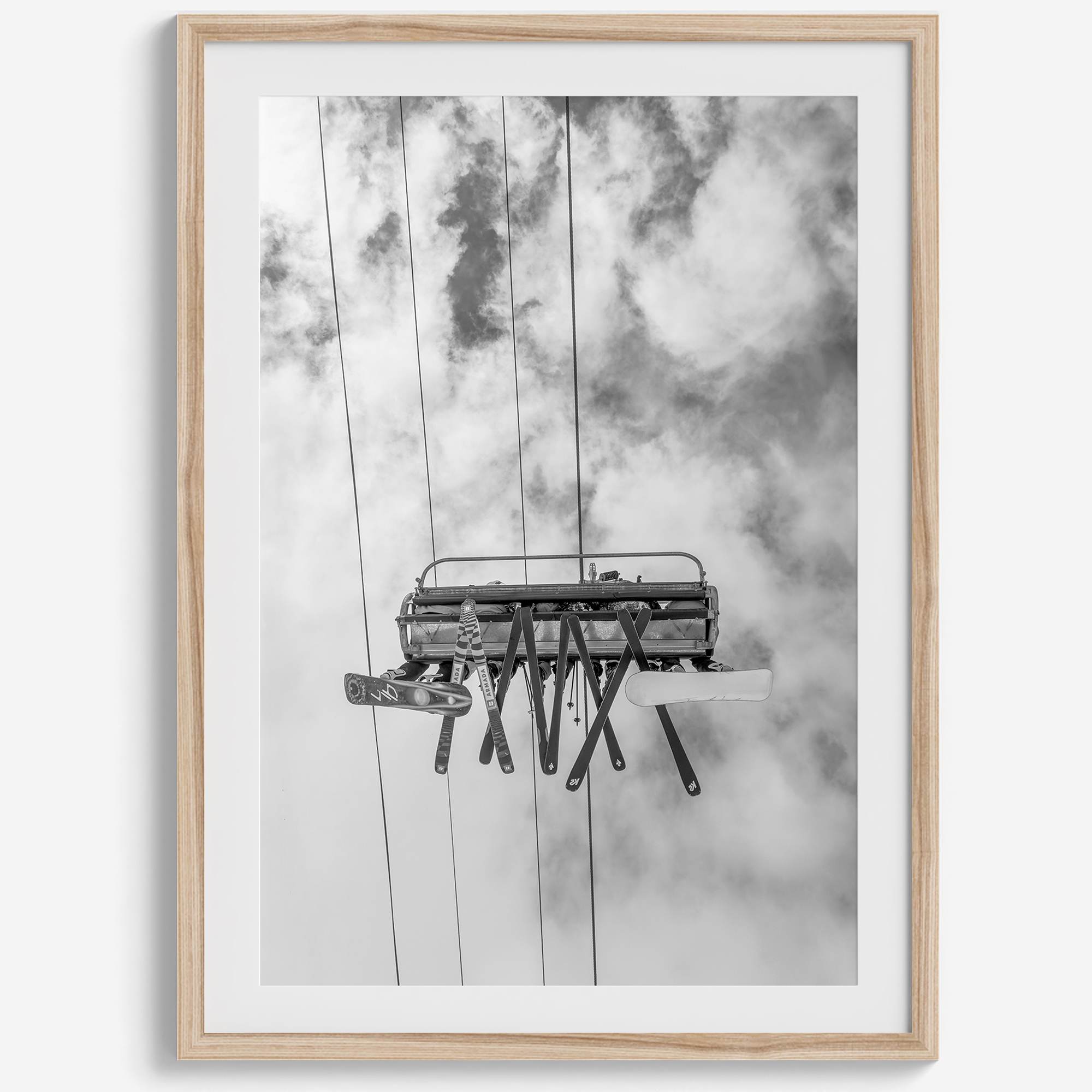 Monochrome ski lift view from below with hanging skis and cloudy mountain sky background.
