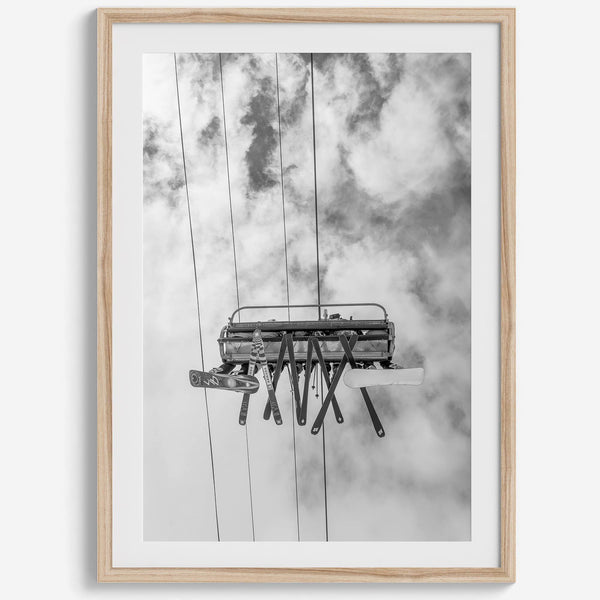 Monochrome ski lift view from below with hanging skis and cloudy mountain sky background.