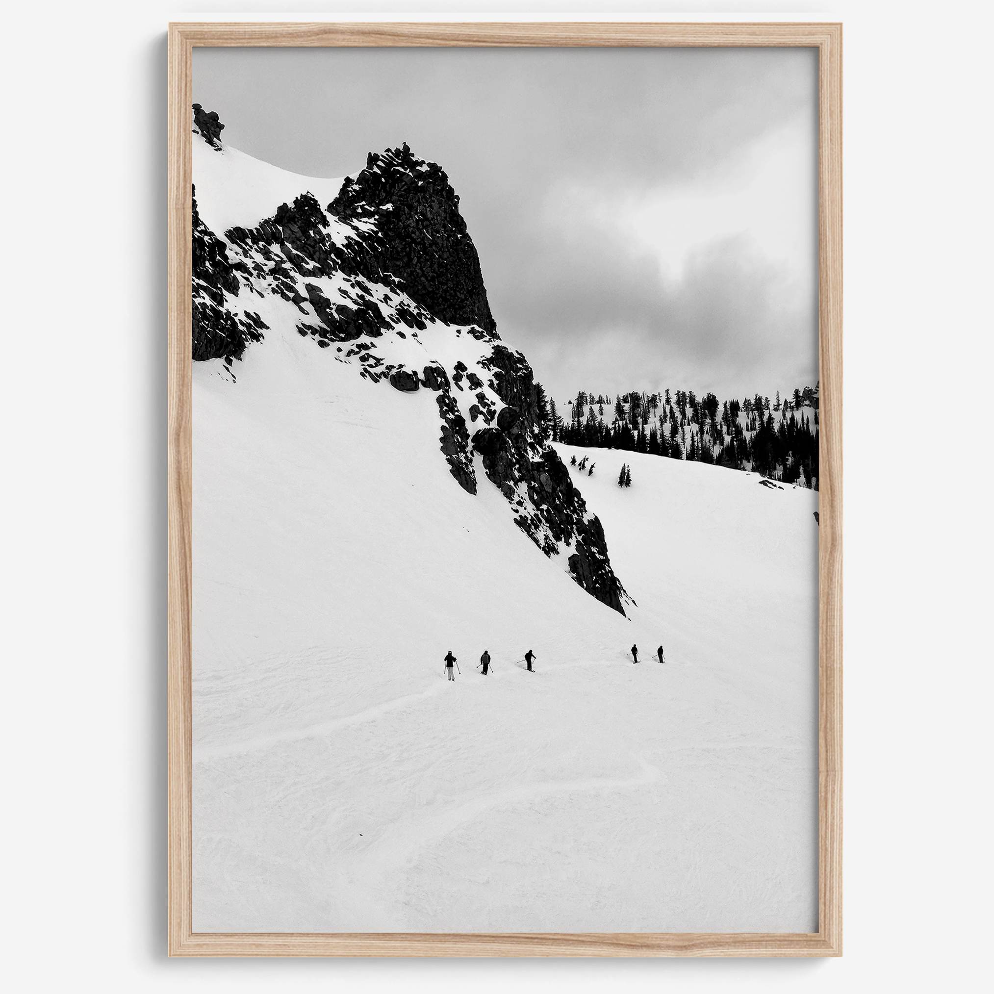 A fine art print showing five skiers traversing a vast, snowy mountain landscape under a pale winter sky, surrounded by untouched wilderness.