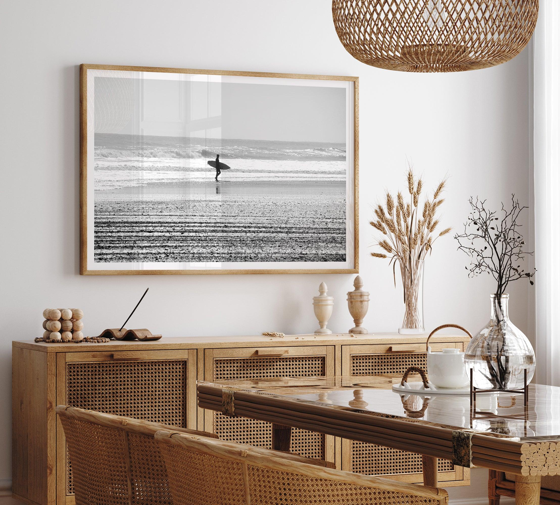 Black and white surfer photography showing a lone surfer on the beach, with waves in the background, capturing minimalist coastal beauty.