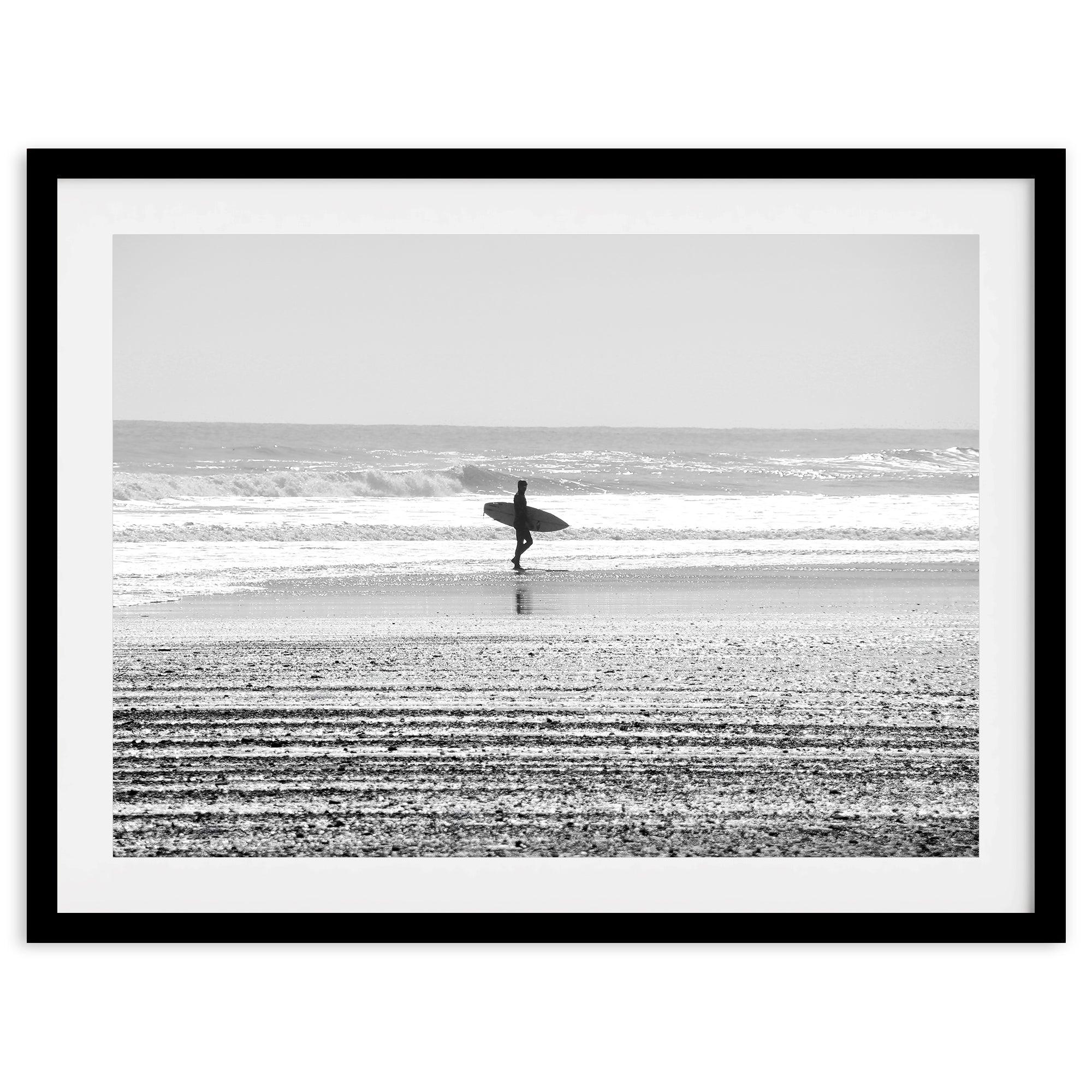 Black and white surfer photography showing a lone surfer on the beach, with waves in the background, capturing minimalist coastal beauty.