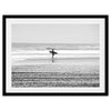 Black and white surfer photography showing a lone surfer on the beach, with waves in the background, capturing minimalist coastal beauty.