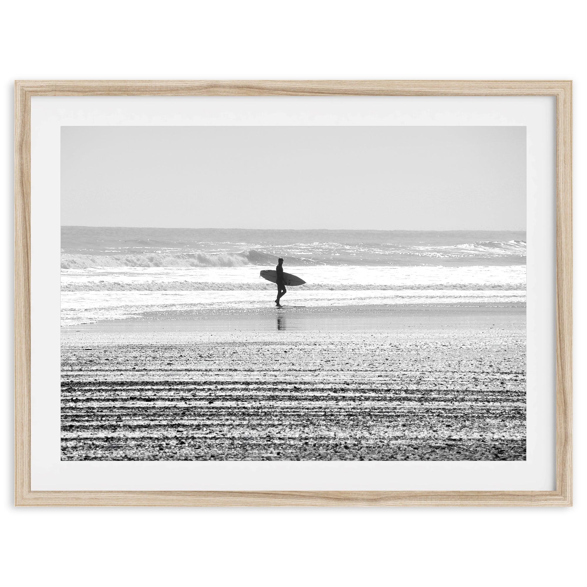 Black and white surfer photography showing a lone surfer on the beach, with waves in the background, capturing minimalist coastal beauty.