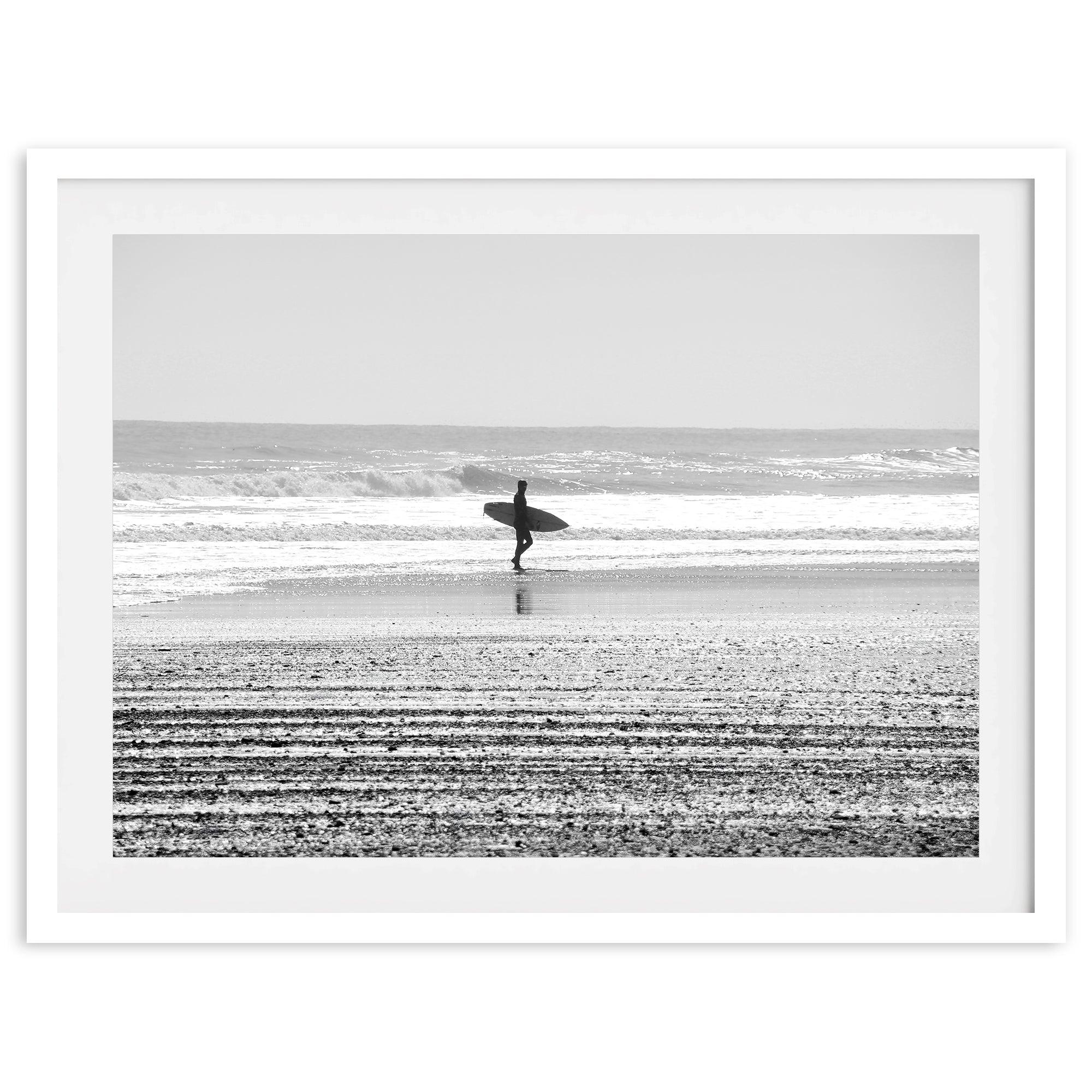 Black and white surfer photography showing a lone surfer on the beach, with waves in the background, capturing minimalist coastal beauty.