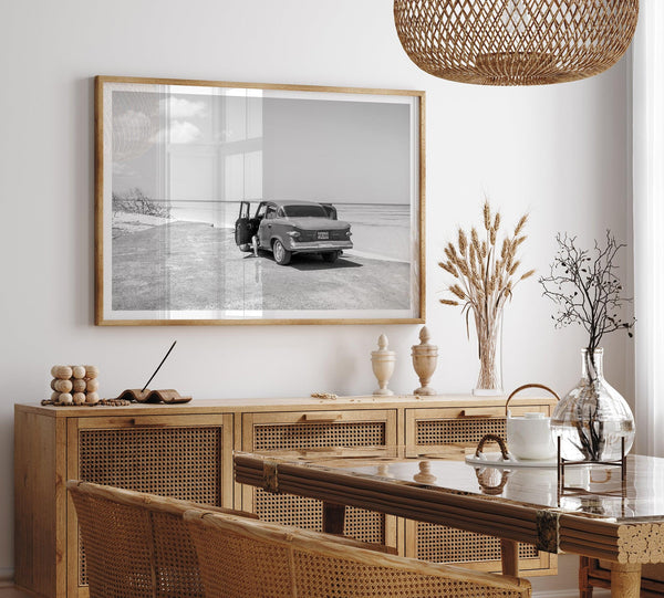 Black and white vintage beach print featuring a classic car parked at the edge of the ocean, capturing a retro coastal scene with timeless charm.