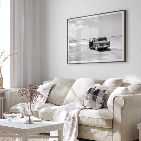 Black and white vintage beach print featuring a classic car parked at the edge of the ocean, capturing a retro coastal scene with timeless charm.