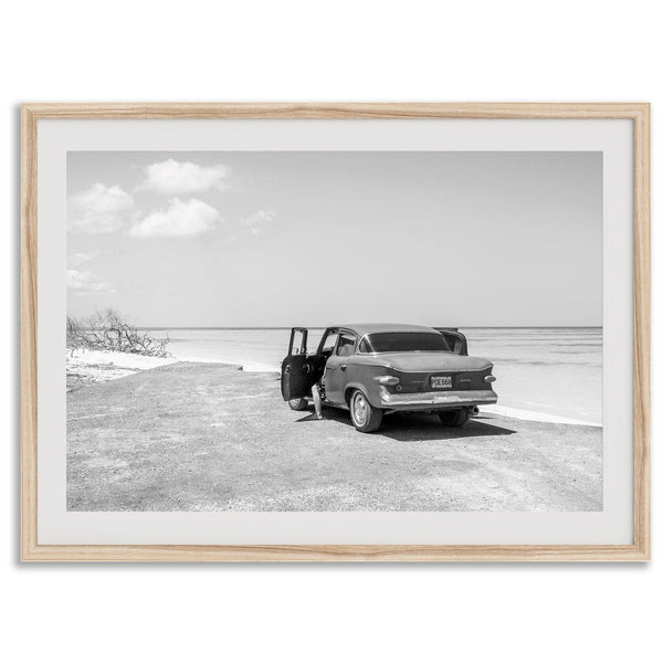 Black and white vintage beach print featuring a classic car parked at the edge of the ocean, capturing a retro coastal scene with timeless charm.