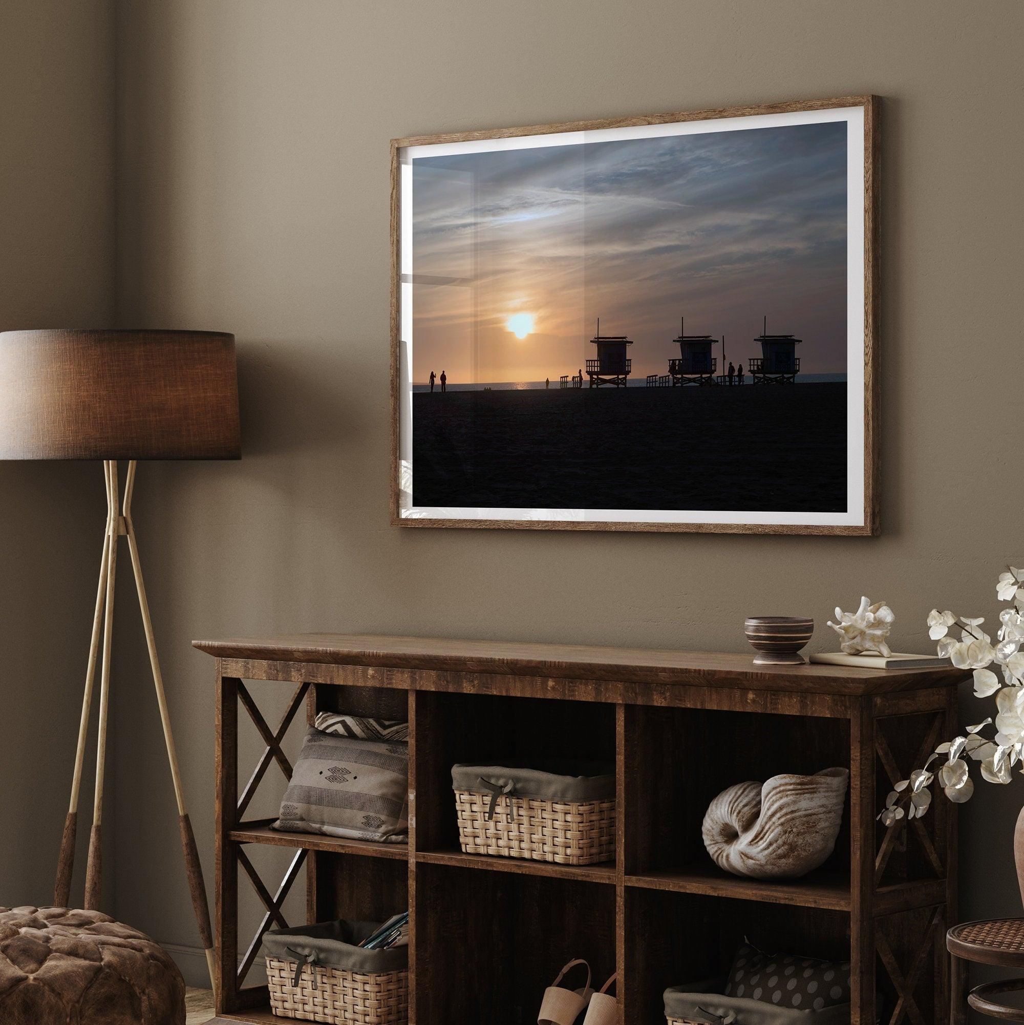 Step into Venice Beach with our fine art beach sunset framed or unframed print. The print showcases the beach in sunset with the silhouettes of the famous lifeguard towers and people in the sunset.