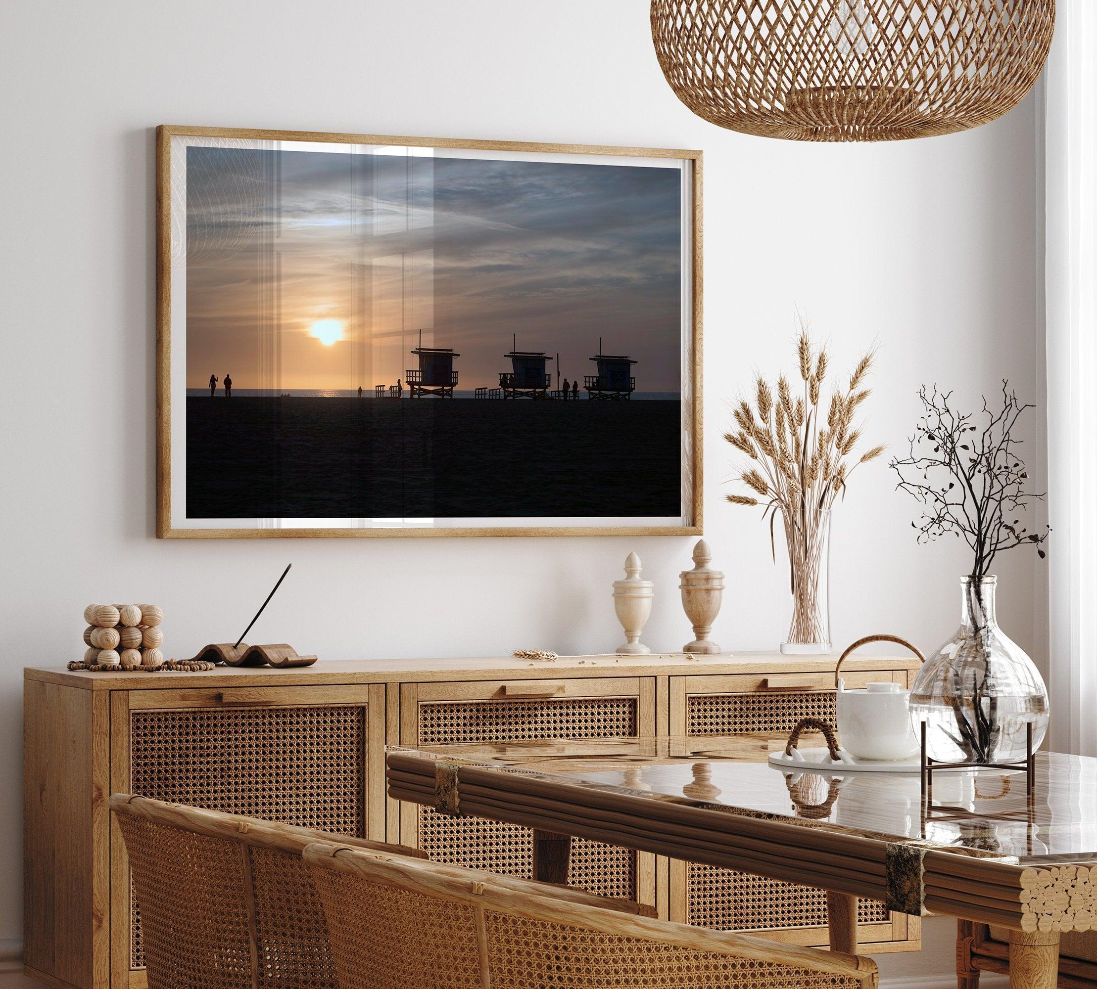 Step into Venice Beach with our fine art beach sunset framed or unframed print. The print showcases the beach in sunset with the silhouettes of the famous lifeguard towers and people in the sunset.