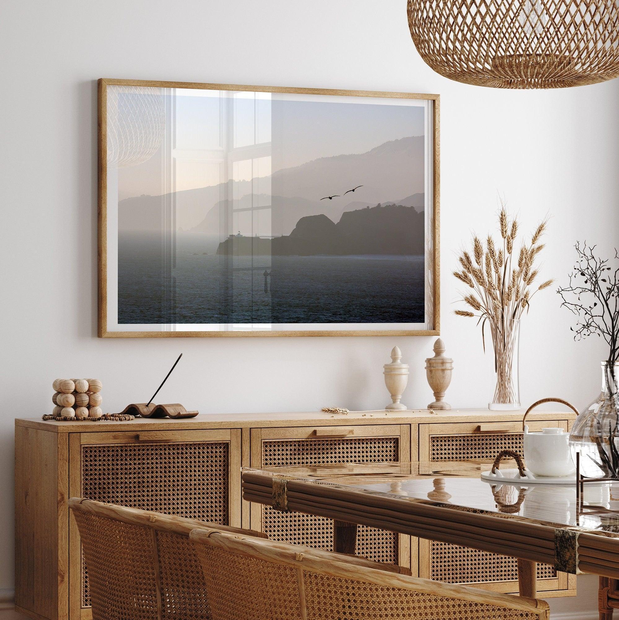 This fine art coastal photography print showcases two birds majestically flying over the Pacific Ocean towards the layered Marin mountains in the sunset. On one of the ridges, there is a lighthouse. The photo was taken from Lands End San Francisco.