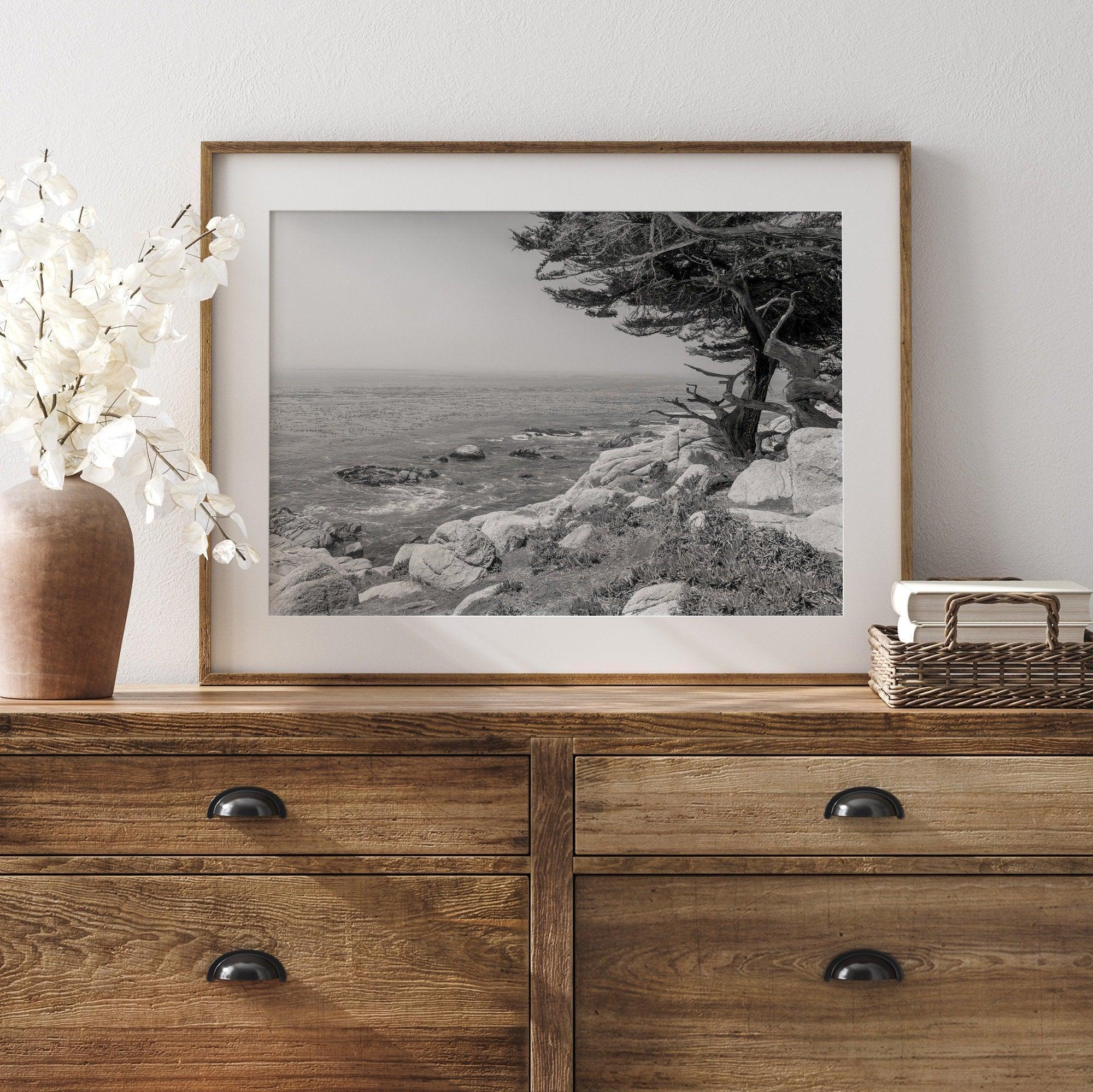 A framed or unframed coastal fine art photography print of a huge cypress tree overlooking the ocean. This black-and-white wall art shows the California rugged coastline in all its glory. Get this Ocean wall decor piece today.